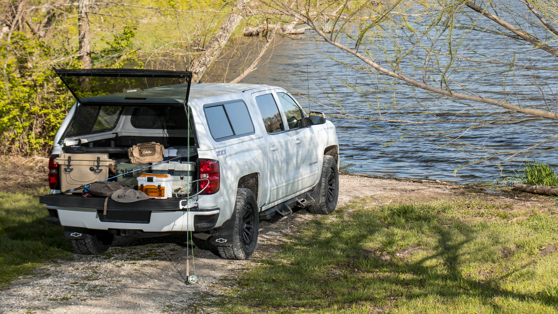 White Chevy Silverado with a Jason truck cap and fishing gear loaded in front of a lake